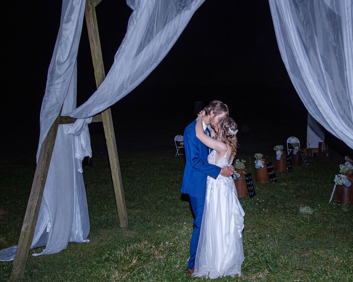 bride and groom kissing after the wedding is over, underneath an arbour with non one watching