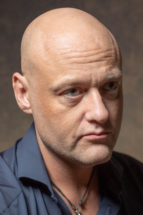 Close-up portrait of a bald man in a navy shirt with soft studio lighting, photographed in Stockholm by Mats Karlsson.