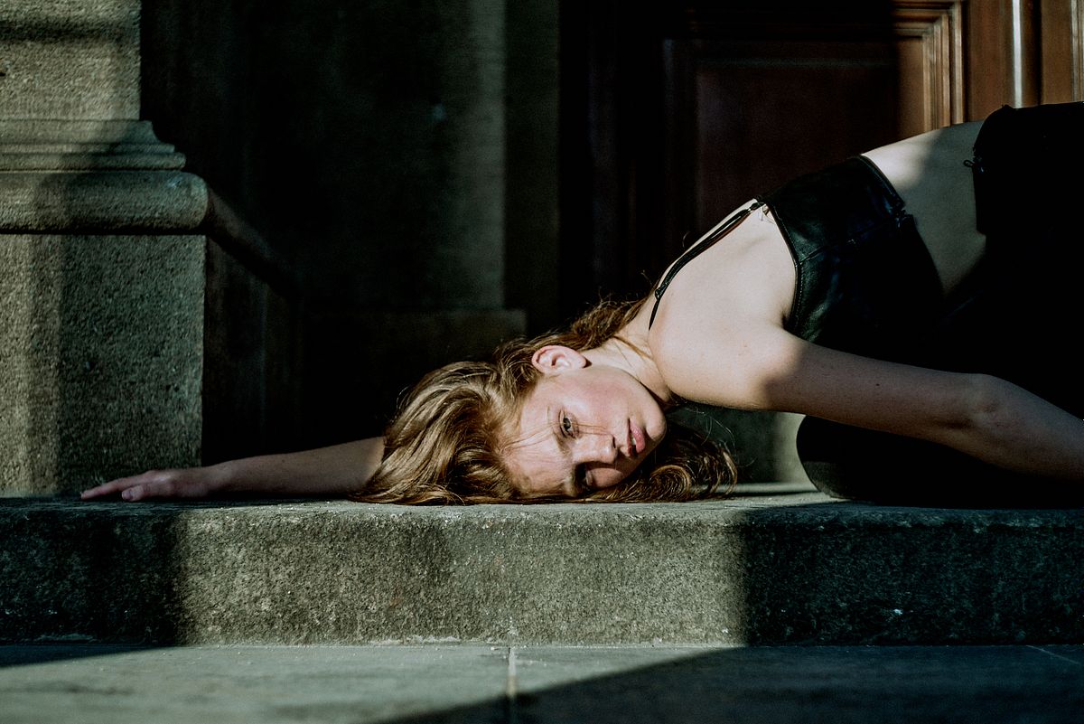 Cinematic editorial portrait of a young woman lying on stone steps in soft natural light, photographed by Gabriel Matula in a poetic fine art style.
