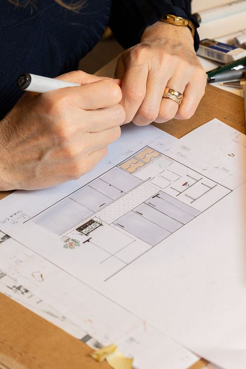 Närbild av händer som skissar en planritning vid bord – inredningsdesign i process.