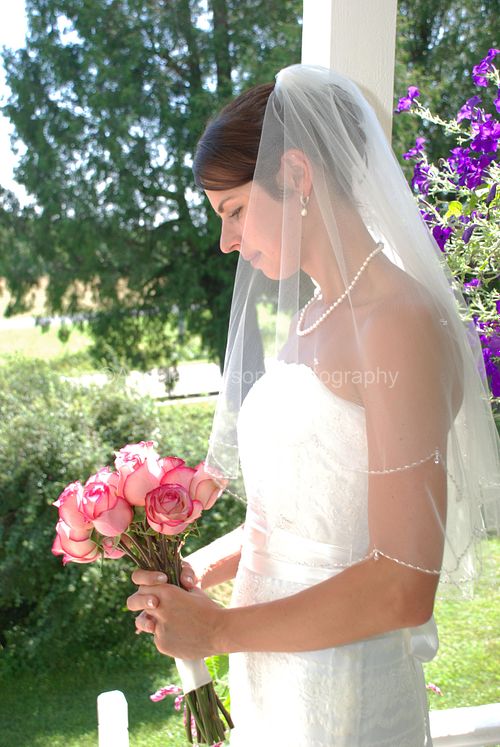 A bride in her veil gazes at her bouquet on the front porch in beautiful sunlight