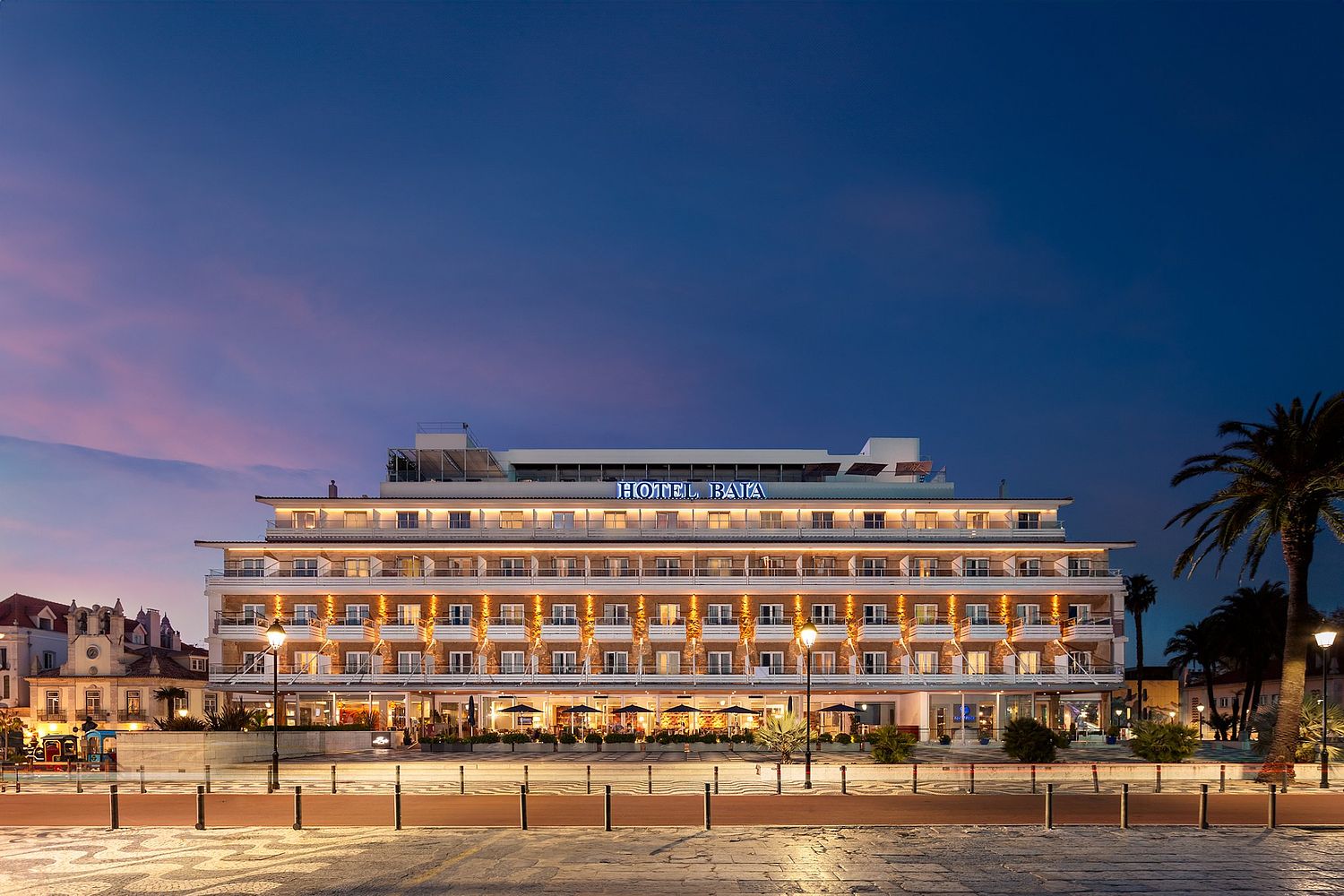 Fachada iluminada do hist&oacute;rico Hotel Ba&iacute;a em Cascais ao anoitecer, fotografada por Pedro Br&aacute;s Photography &mdash; fotografia profissional de arquitetura e hotelaria em Portugal, com especializa&ccedil;&atilde;o em reportagens de hot&eacute;is de luxo e patrim&oacute;nio hist&oacute;rico.