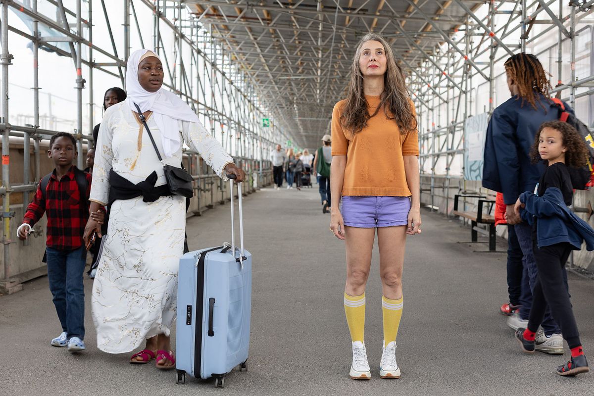 Kvinna st&aring;r mitt i g&aring;ngtunnel medan m&auml;nniskor med bagage passerar