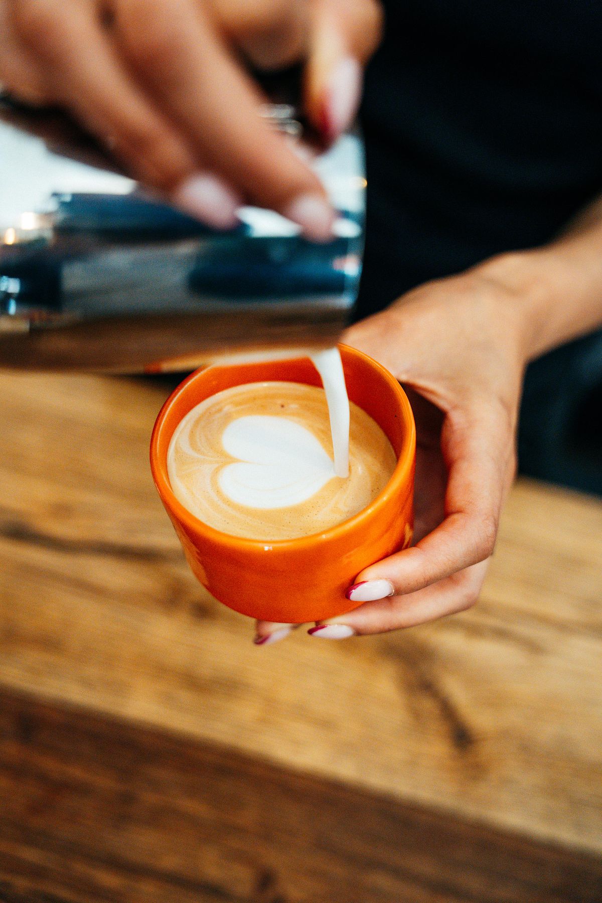 barista creating a coffee in a orange ceramirk cup