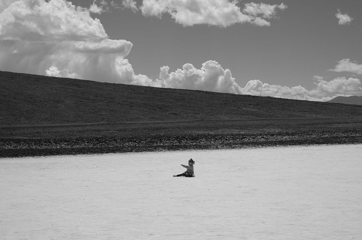 A lone figure sitting in a vast open space under a dramatic cloudy sky, captured by photographer Sandeep Gajula