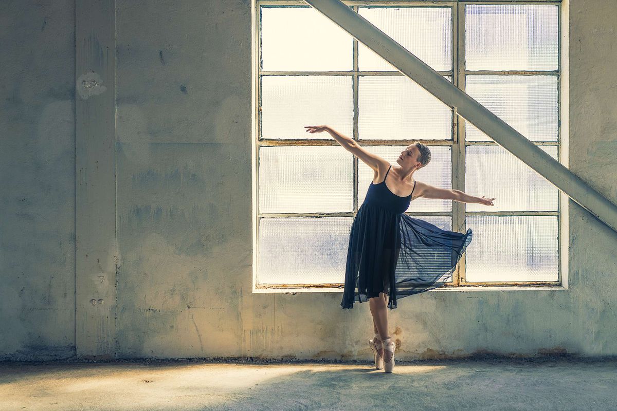 femme en robe de ballerine noire dans bâtiment industriel, sur pointes, éclairée par la lumière naturelle, photographie artistique