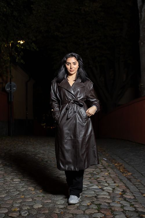 Helfigursporträtt av skådespelare i mörk läderkappa i kvällsmiljö, fotograferat i stadsmiljö med dramatiskt ljus.