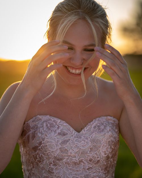 Portrait of Prince Albert Grad smiling and lifting her hands to her face during golden hour.