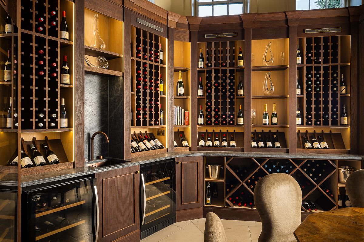 Interior view of a wine cellar and tasting area at Carton House, a Fairmont Managed Hotel. Features custom-built dark wood cabinetry by FJS Joinery, with wine racks, shelving, refrigerated units, and a countertop with a sink.