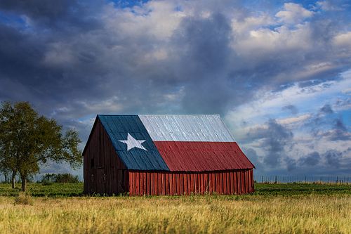 A horizontal view of the iconic Texas Flag barn in Bruce-Eddy under dramatic, stormy blue clouds