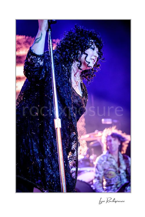 Vertical color image of Ann Wilson at the microphone during a Heart concert, wearing black stagewear under vivid purple and blue stage light