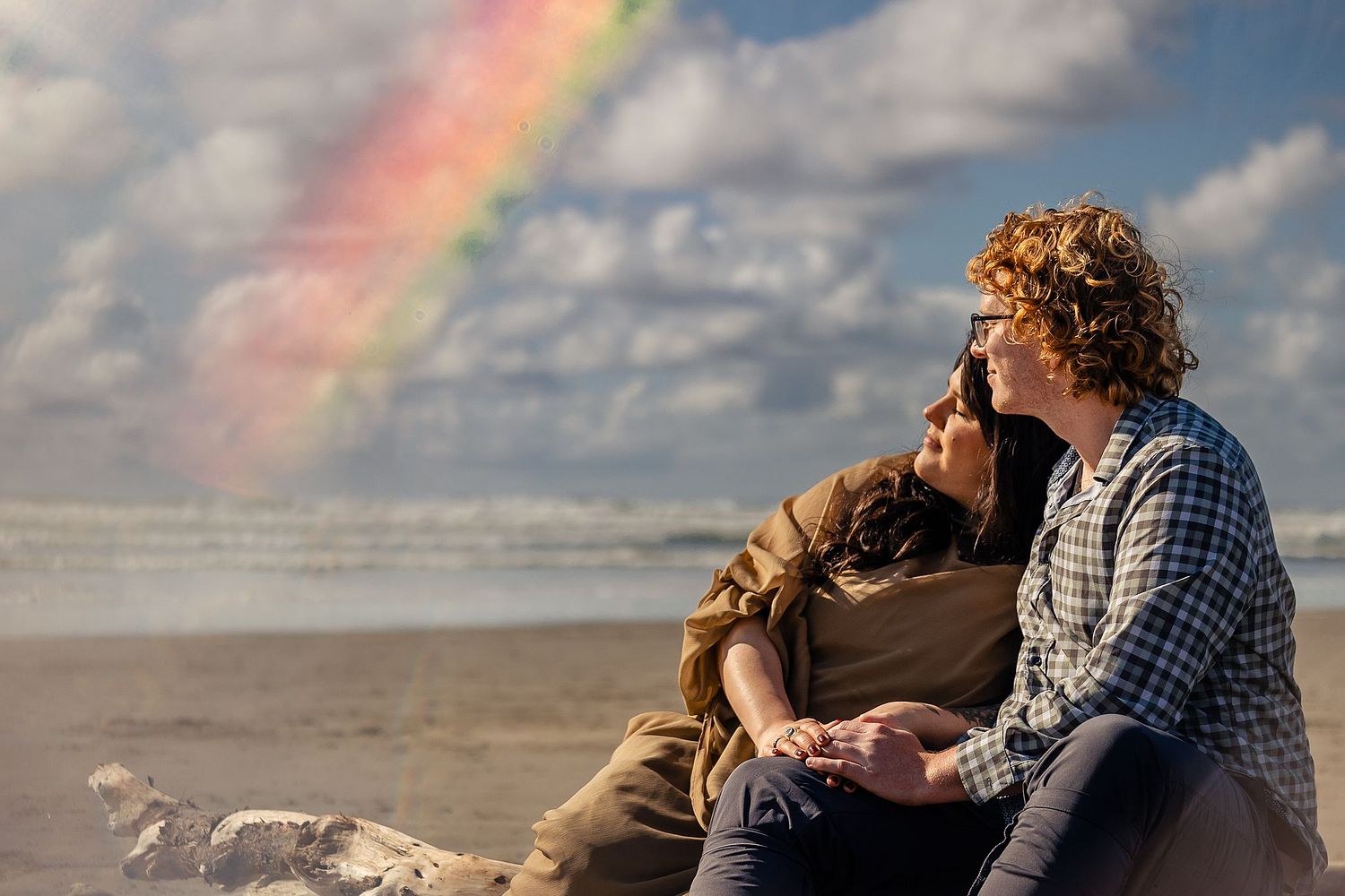 A couple cuddling on the beach with a rainbow prism above them