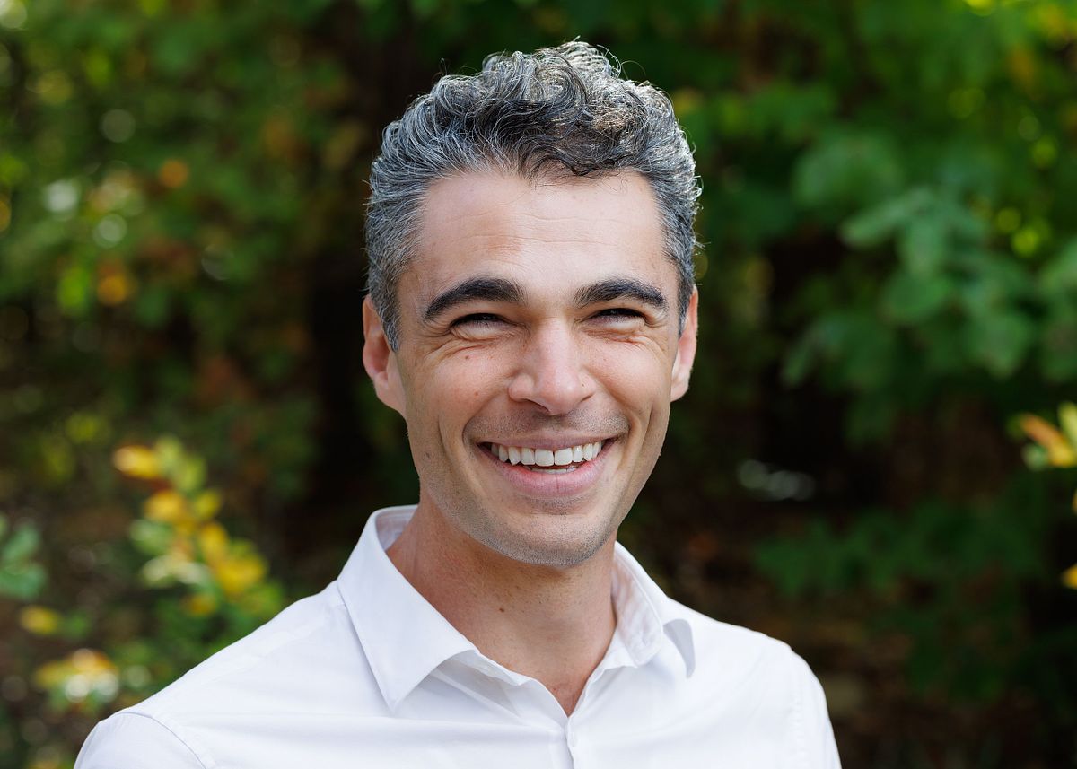 A close-up headshot of a man against a wooded backdrop at UNC's campus in Chapel Hill, NC