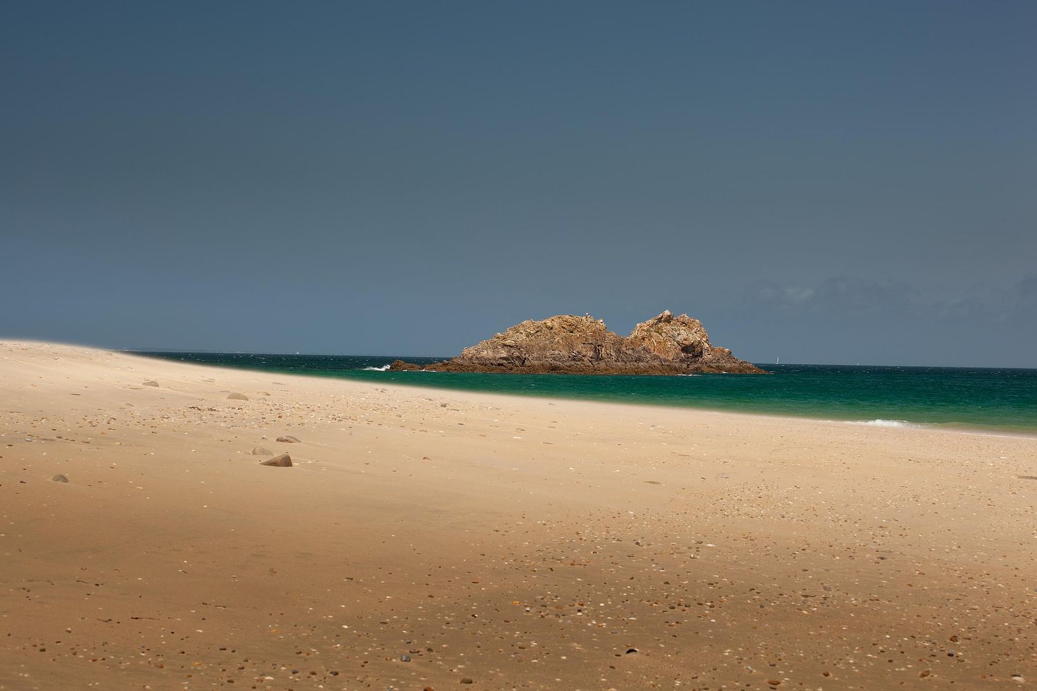 A heavenly view of the beach a rock and the turquoise sea.
