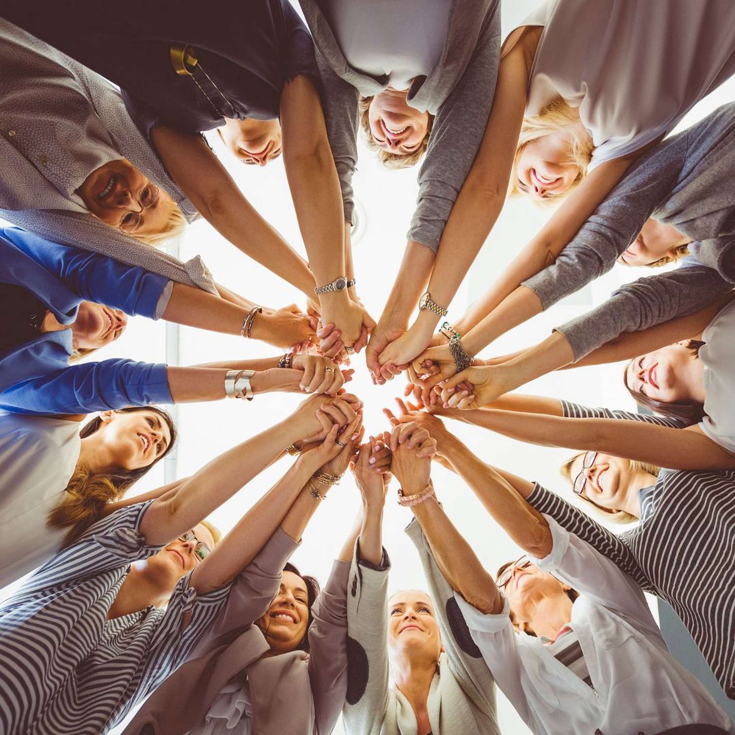view from below of a circle of women all joining hands in a huddle