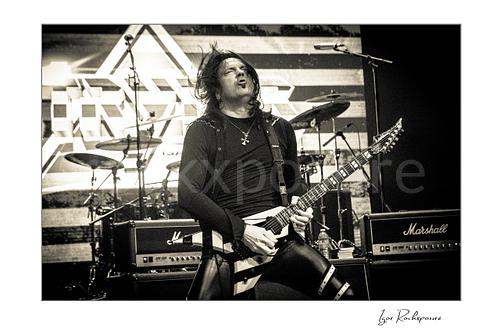 Horizontal black and white image of Michael Sweet of Stryper performing live with a striped electric guitar on stage