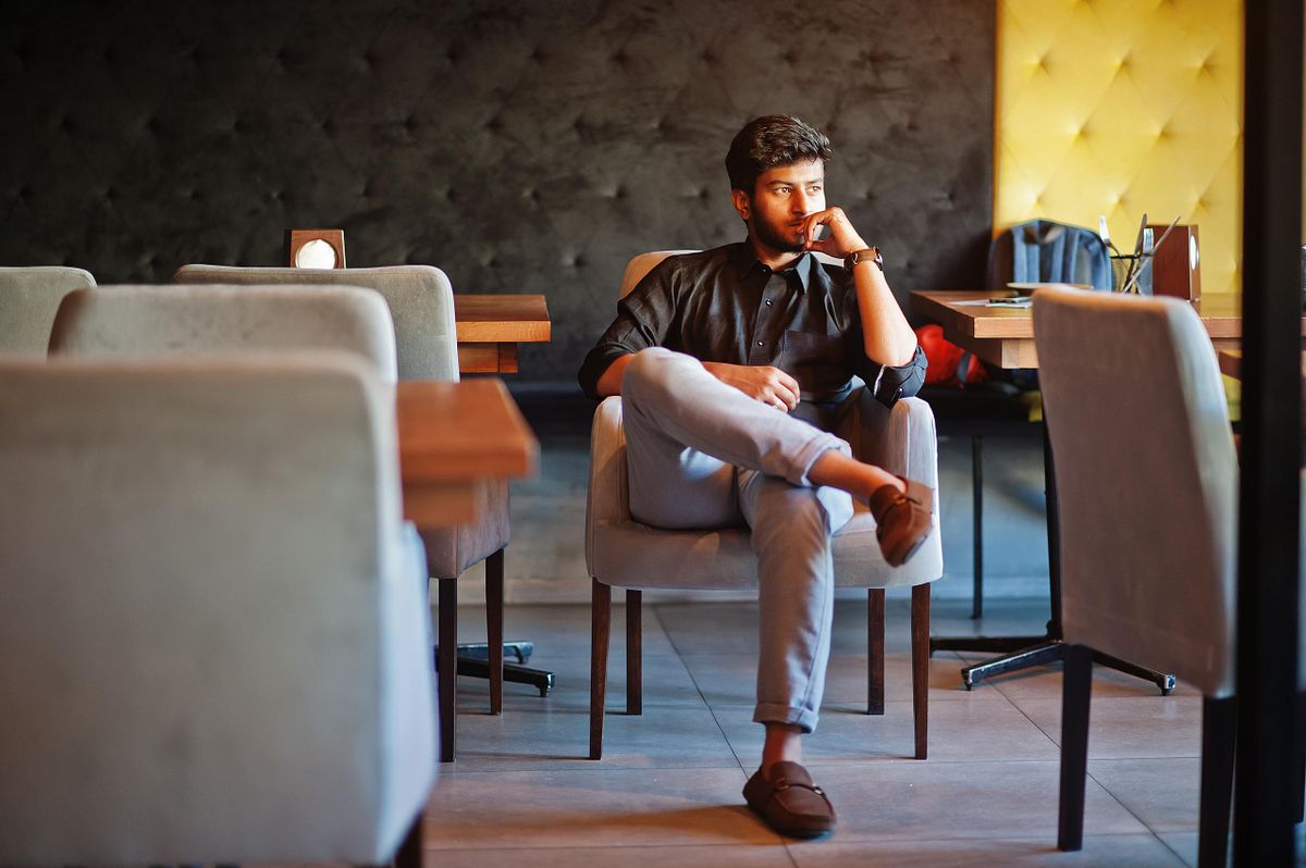 Confident young indian man in black shirt sitting at cafe.