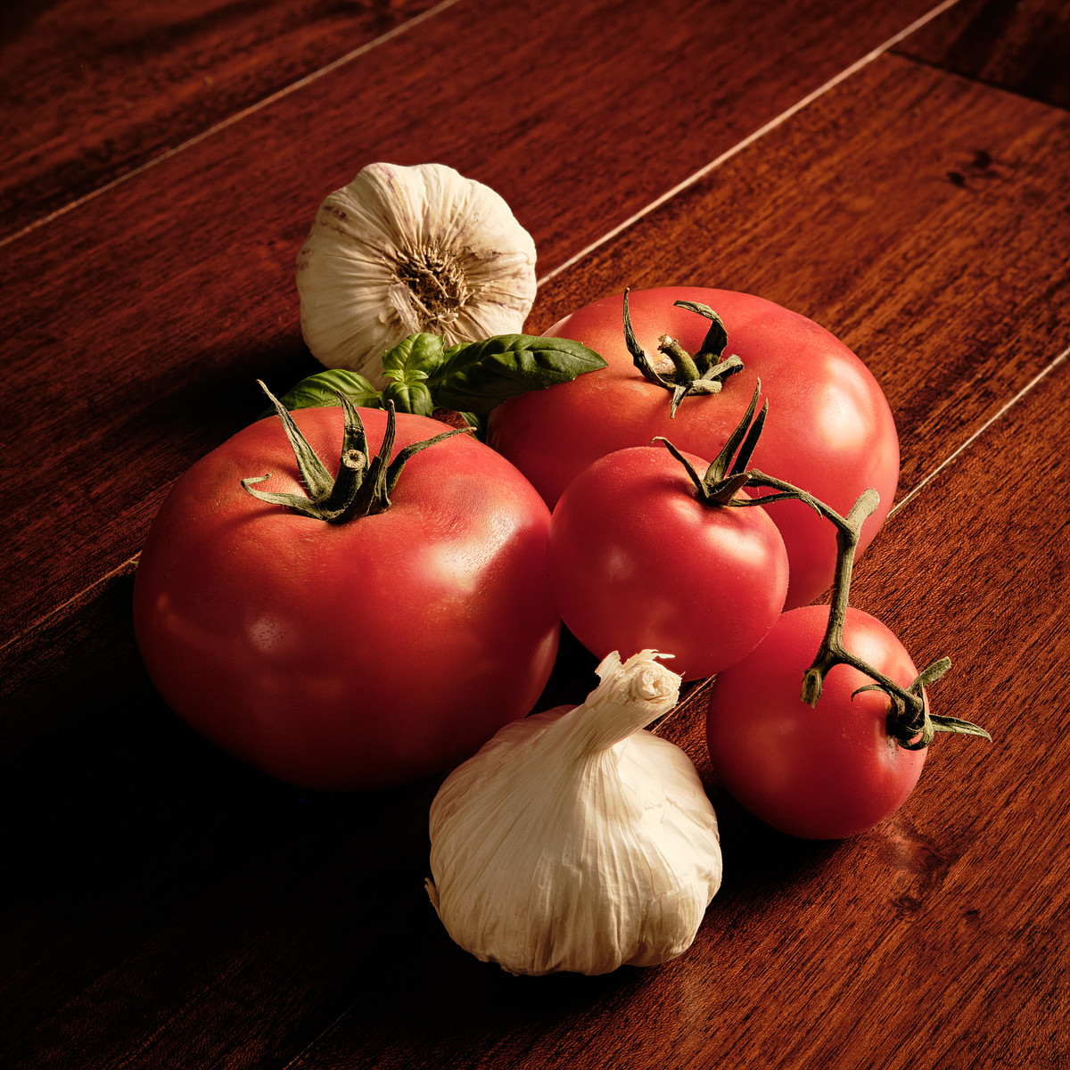 Several red tomatoes and garlic on mahogany wood.