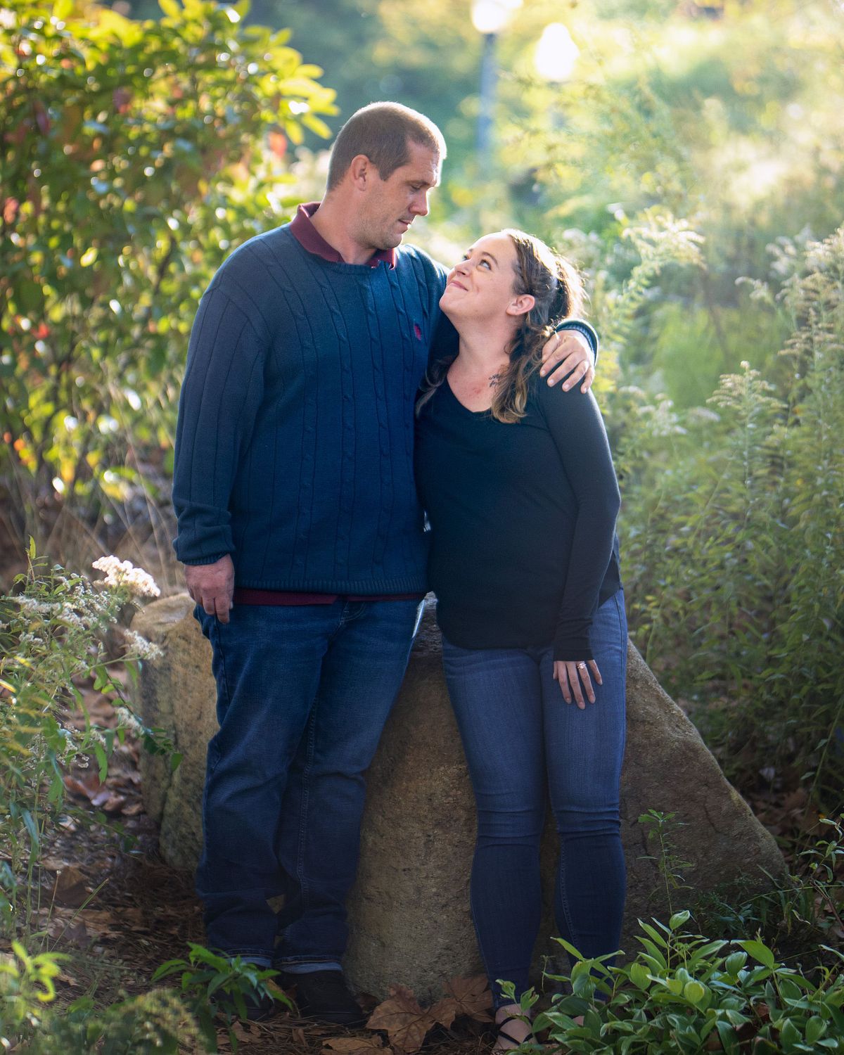 marriage proposal at quiet waters park in annapolis maryland, the couple are posing in front of a big rock surrounded by foliage with the sun being backlit