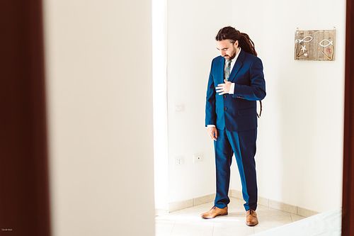 "scatto rubato di sposo che si guarda l'abito azzurro che indossa colto da una altra stanza"