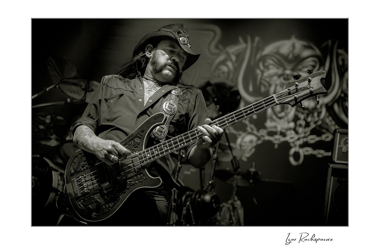 Horizontal concert photography of Lemmy Kilmister playing bass guitar in black and white concert photography under stage lighting