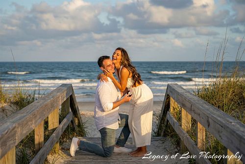 A joyful couple celebrating a spontaneous beach proposal on a wooden boardwalk at sunset in Northeast Florida.