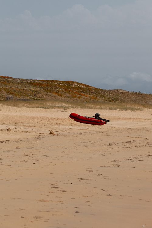 Bateau rouge posé sur plage mouillée.