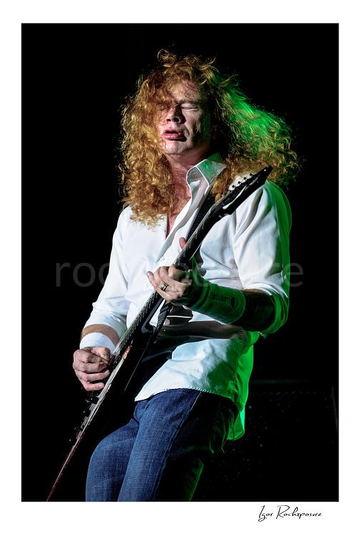 Vertical color image of Dave Mustaine of Megadeth playing guitar on stage with curly red hair and green stage light