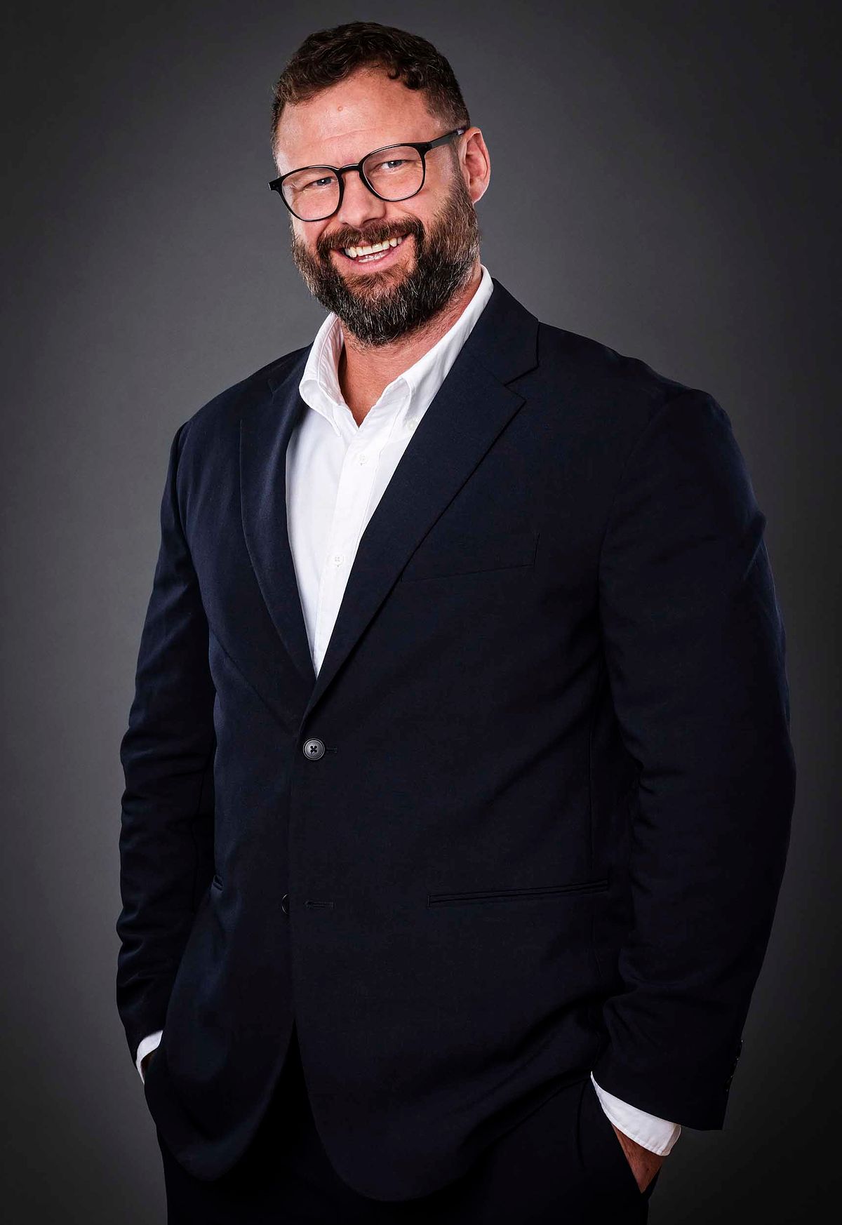 Corporate portrait of James Morris from Ambrose Finance. Dark grey background. wearing a suit.