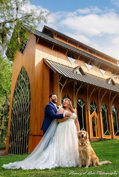 A joyful bride and groom smiling with their golden retriever dog in front of the historic Baughman Center chapel in Gainesville, FL.