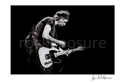 Horizontal black and white image of Keith Richards of The Rolling Stones performing live with electric guitar in a dramatic stage portrait