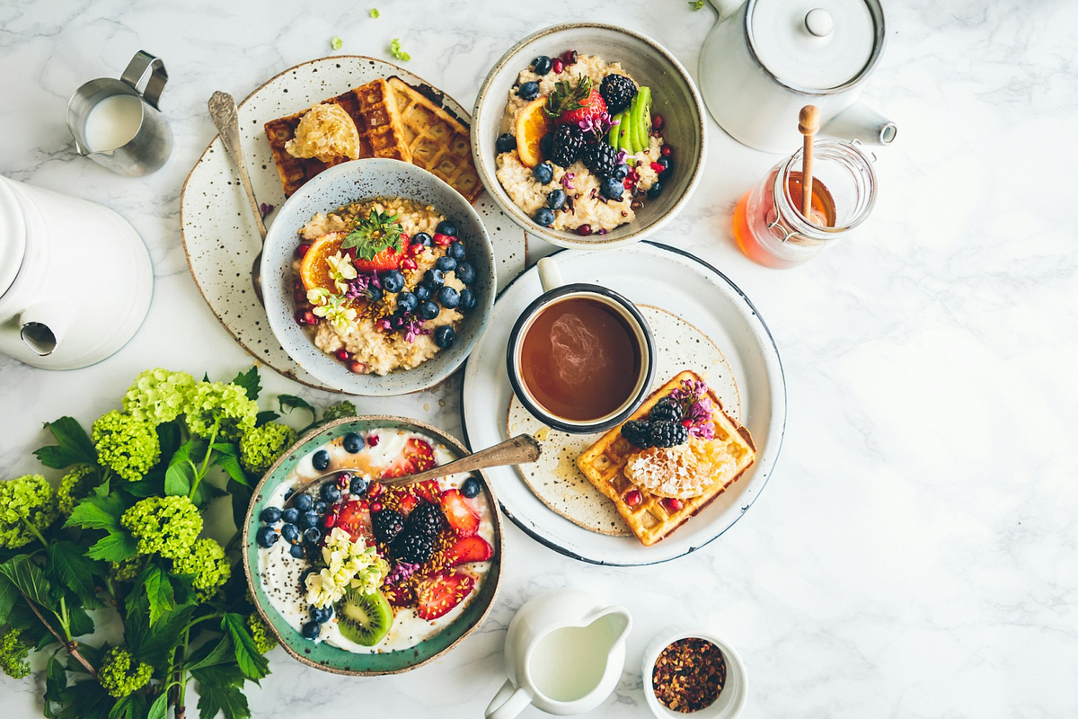 a healthy breakfast including waffles, fruit bowls and tea on a white marble table