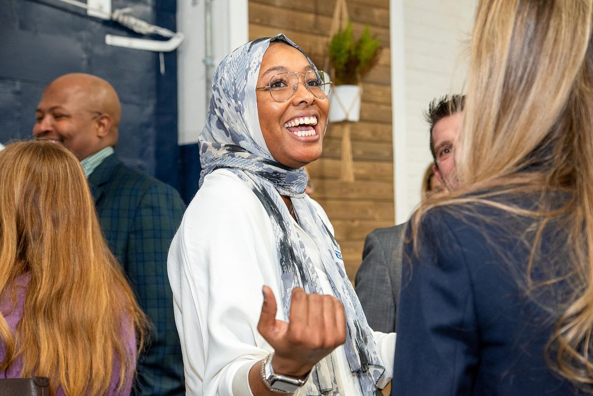 Professional woman in patterned hijab smiling and engaging in conversation during a corporate networking event, captured by Andriana Ortiz for Embassy Interactive.