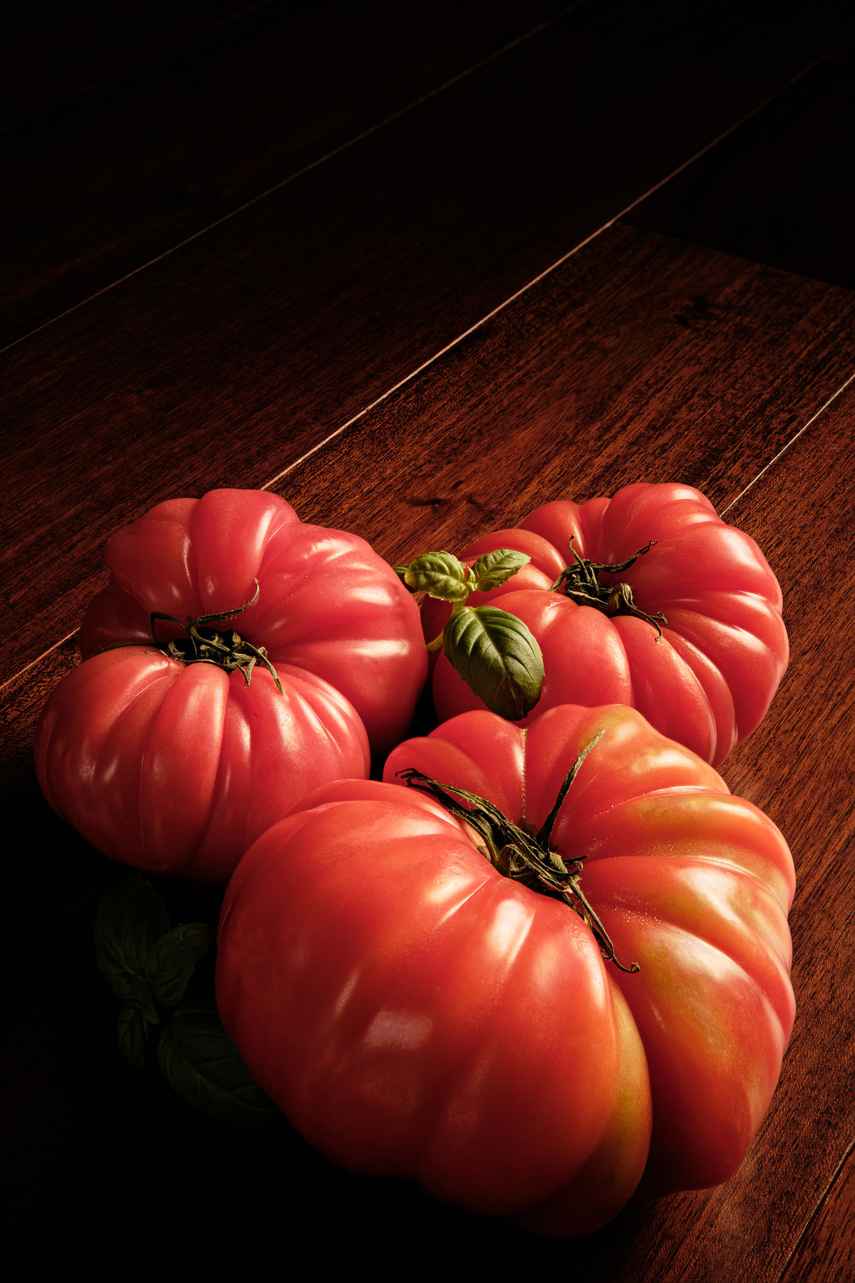 Three red heirloom tomatoes on mahogany wood.