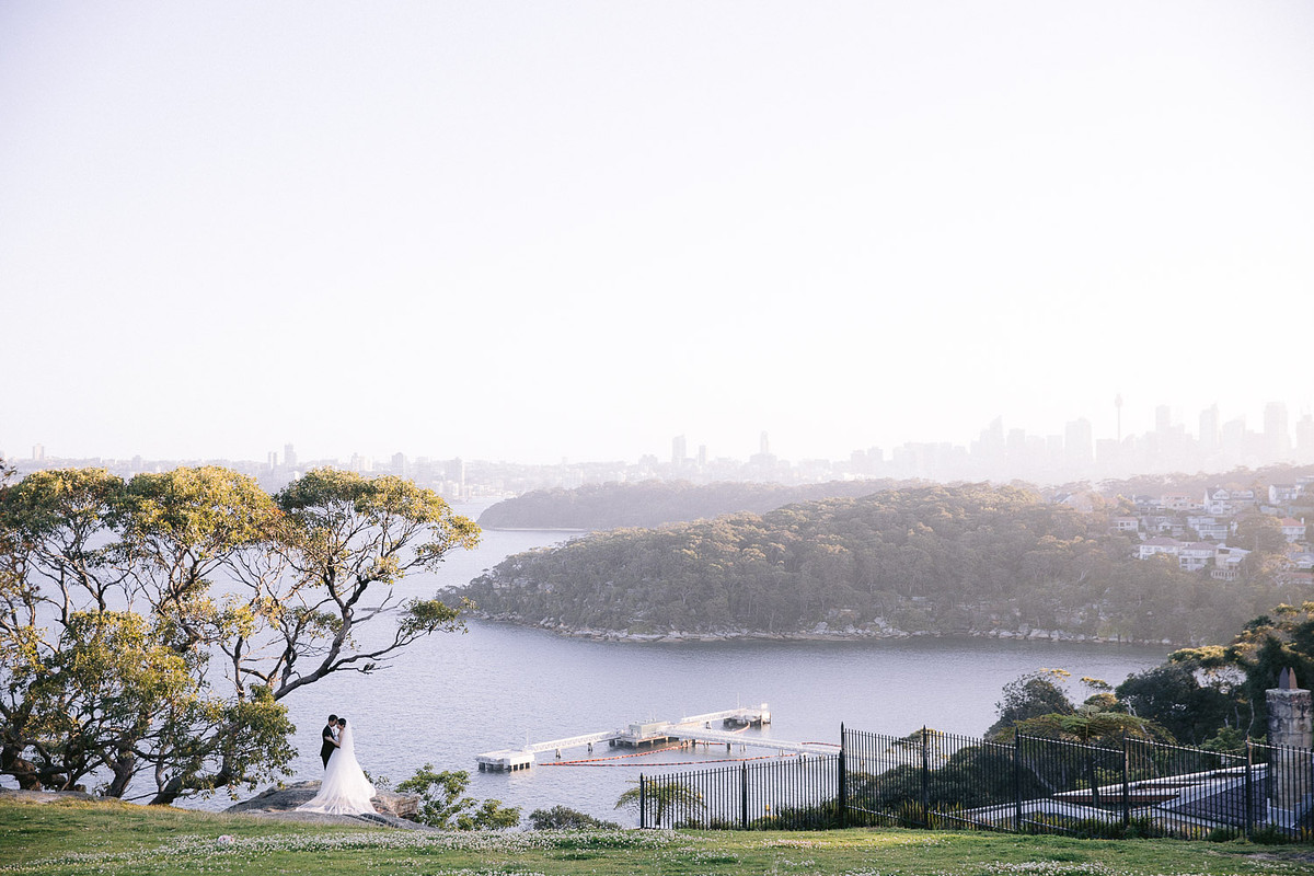 Scenic wedding photo of the newlyweds standing under the tree with a breathtaking backdrop of Sydney Harbour at Georges Head Lookout