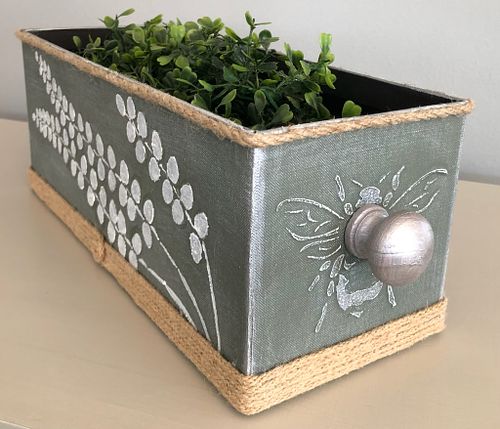 Decorative drawer with botanical design and a silver knob, filled with greenery.