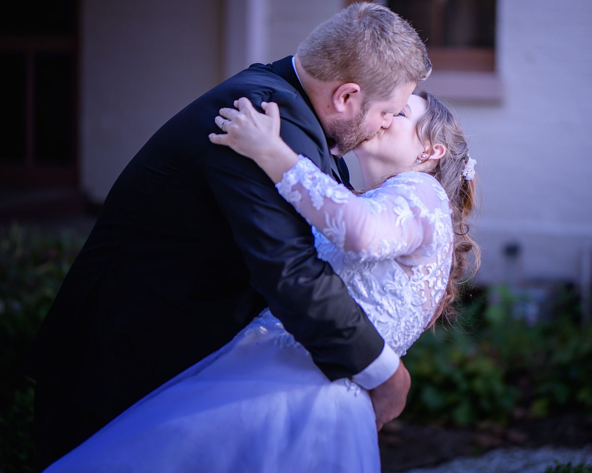 groom is kissing his bride while tipping her at ross mansion during golden hour