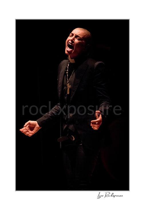 Vertical color image of Sinéad O’Connor singing on stage in a dramatic low-light portrait