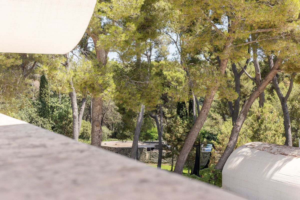 Bes&ouml;kare i skulpturpark med stenmur och stor abstrakt skulptur i soligt dagsljus.