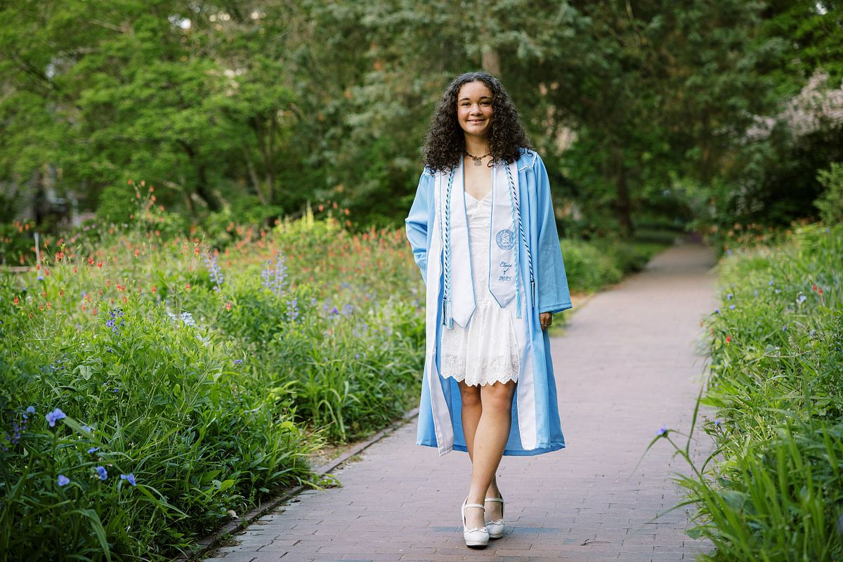 A woman in her graduation robe and stole at the Coker Arboretum on UNC's campus in Chapel Hill, NC