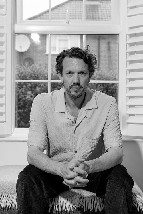 Black and white portrait of a man sitting indoors in front of a window, photographed in London by Mats Karlsson.