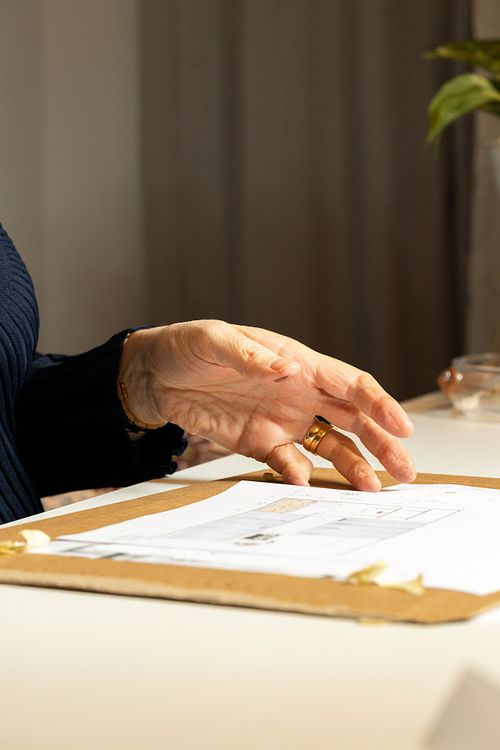 Hand som gestikulerar över ritning på bord, som del av planering och inredningsdesign.