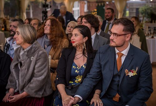 Wedding guests looking on with smiles as they watch the bride and groom, captured by Weddings By Jermaine. The couple is not in the shot, but their presence is felt.