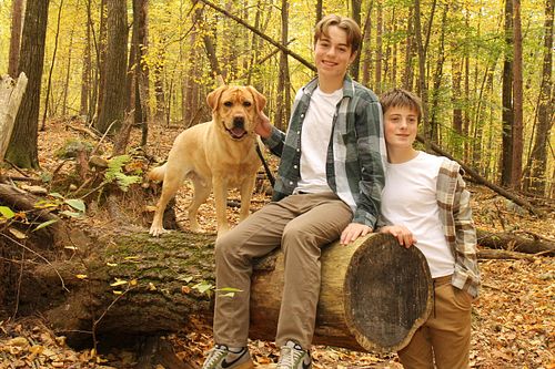 Two teens pose in the woods on a log with their dog