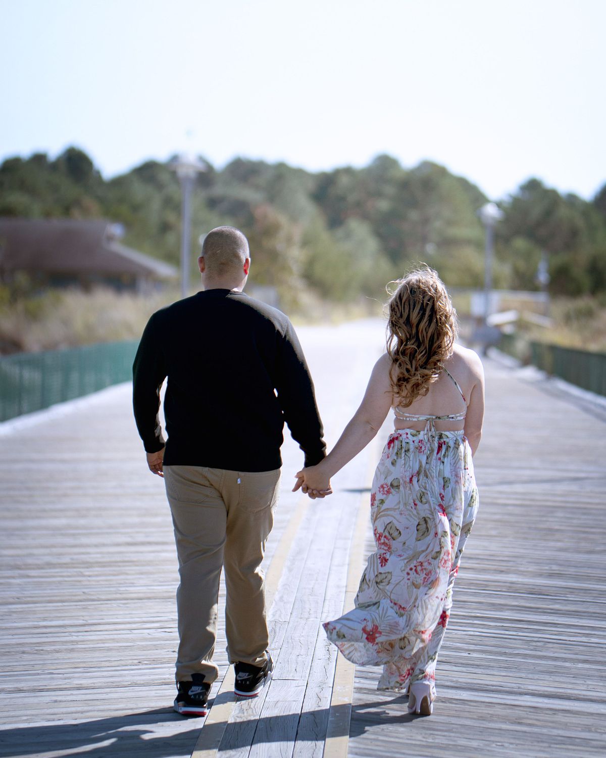 couple walking on the pier at cape henlopen, she is wearing a flowery sundress, they are holding hands