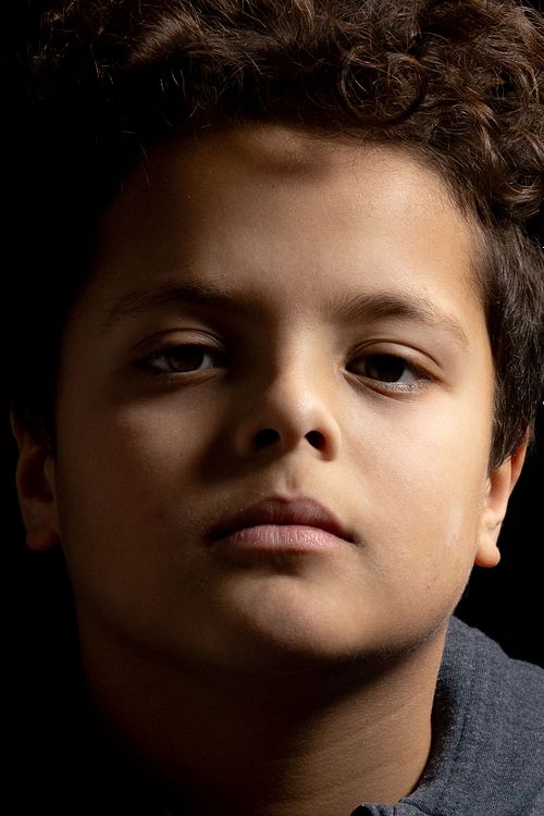 Close-up porträtt av pojke i lågmält studioljus, seriös blick