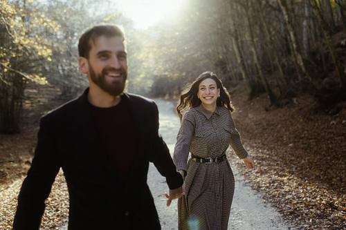 Coppia che corre sorridendo lungo una strada nel bosco marchigiano, gesto spontaneo e atmosfera giocosa.