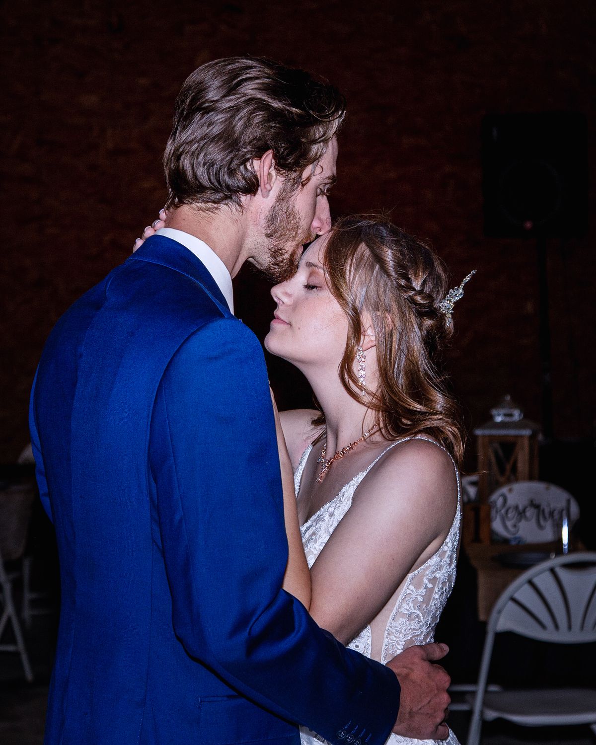 barn wedding documented using flash, the groom is kissing the bride on the forehead and her eyes are closed
