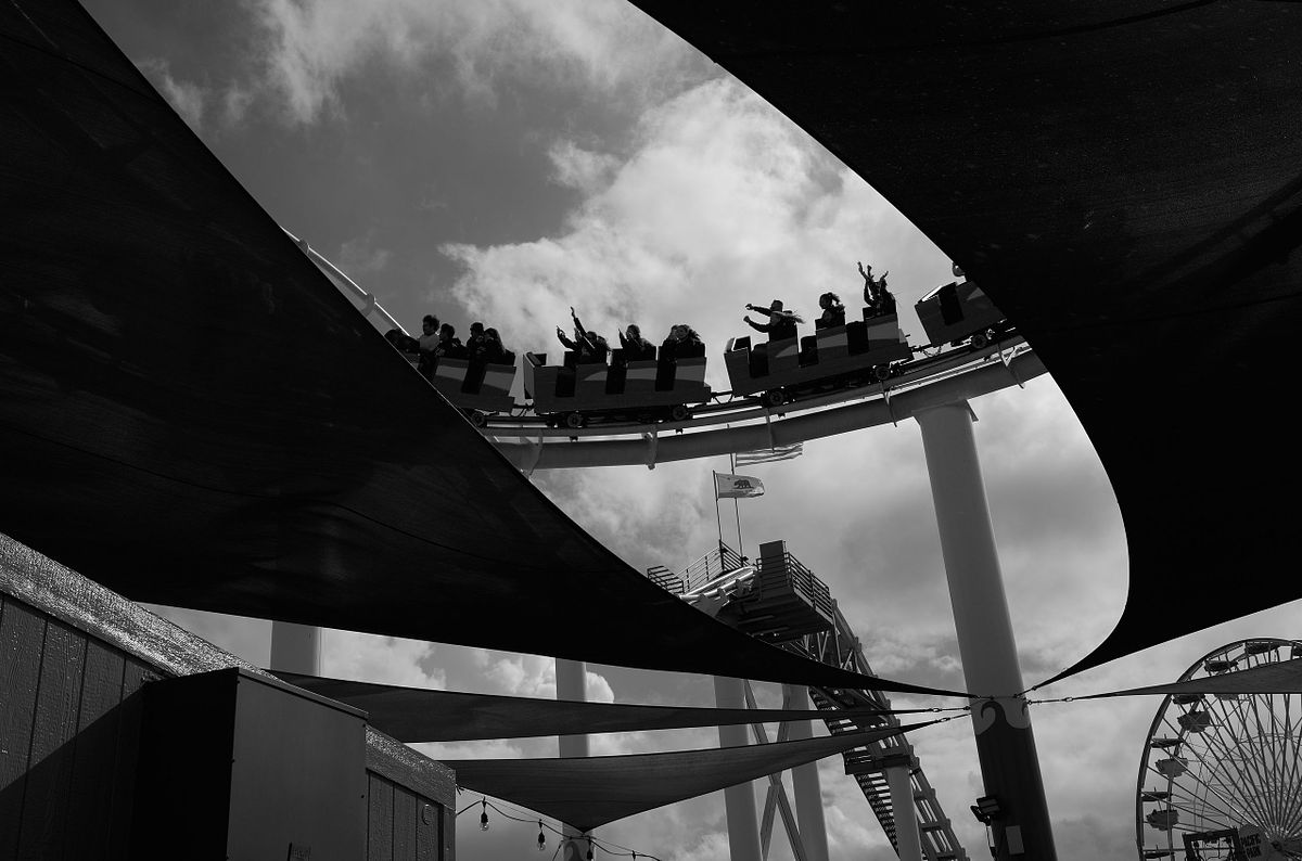 People enjoying a roller coaster ride at Santa Monica Pier under dramatic clouds, captured by photographer Sandeep Gajula