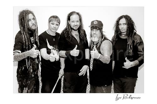 Horizontal black and white image of Korn members posing together in a backstage hallway portrait